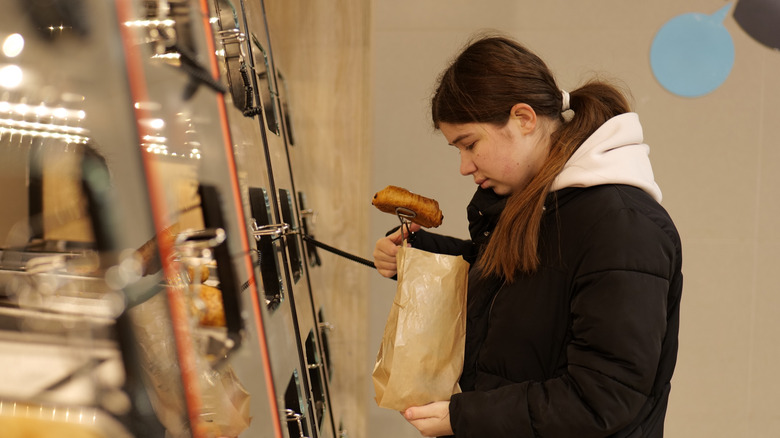 Woman adding pastry to bag at self-service bakery case