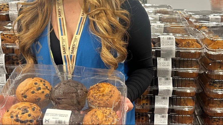 Sam's Club employee holding 6-pack of muffins with muffins in the background