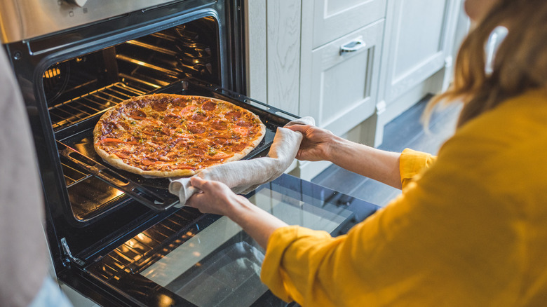 Woman taking pizza out of oven at home