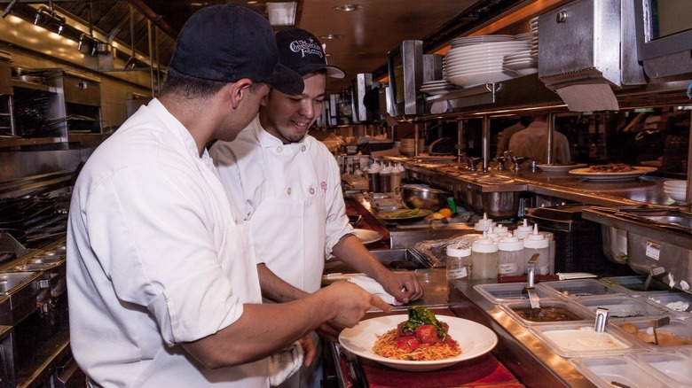 Two Cheesecake Factory chefs in a kitchen with blue caps on