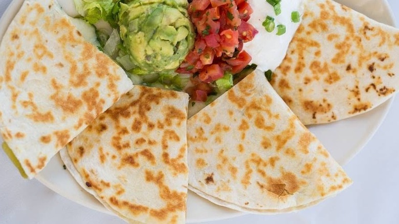 Four quesadillas with garnish on a white plate