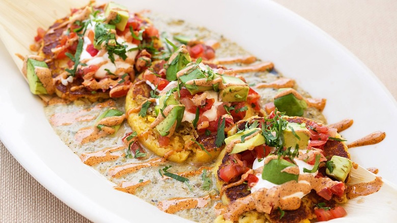 Three sweet corn tamale cakes in a sauce in a white dish