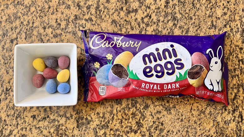 Cadbury Mini Eggs Dark Chocolate inside a white dish and with a wrapper on the side laid on countertop