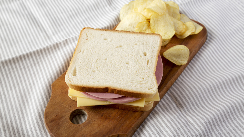 Bologna and cheese sandwich on a rustic wooden board with potato chips