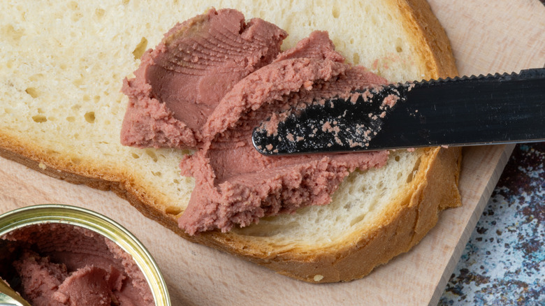 Close-up of a knife spreading liverwurst on bread