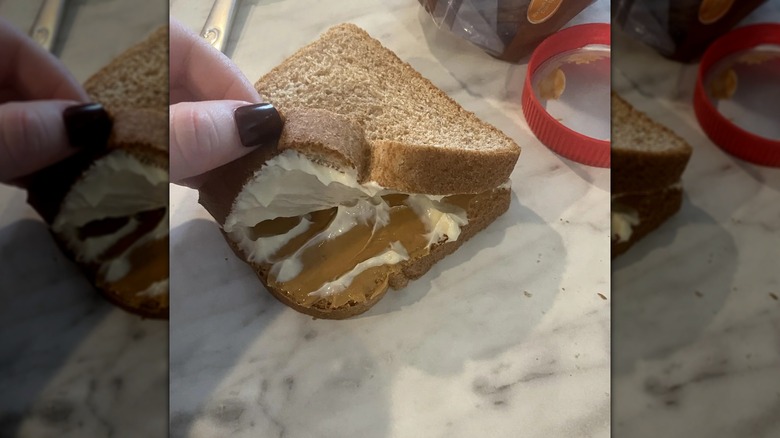 Close-up of a hand opening a peanut butter and mayonnaise sandwich on a marbled table