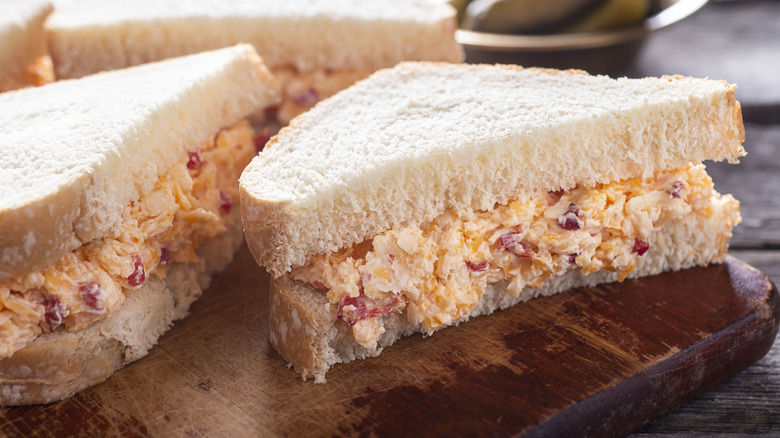 Pimento cheese sandwiches on white bread, cut in half on a wooden board