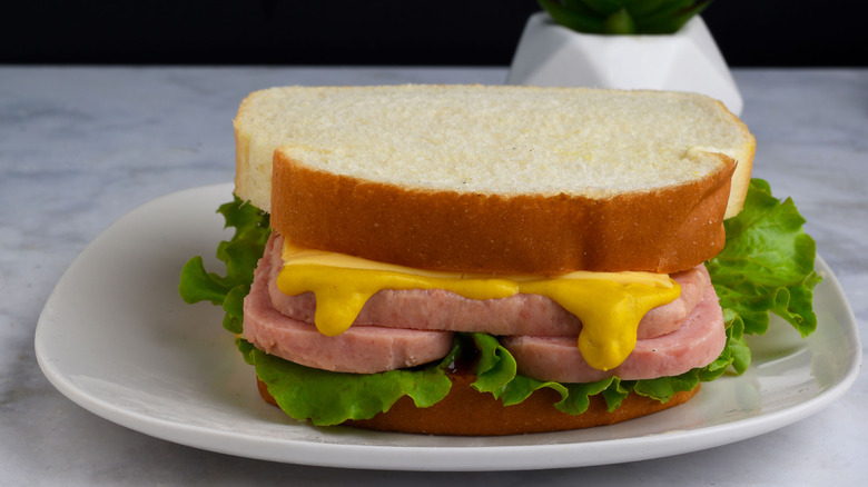 Spam on white bread sandwich with mustard and lettuce on a white plate