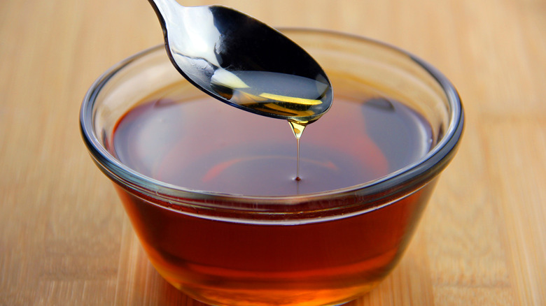 Syrup dripping off of spoon into a glass bowl on a bamboo wooden table