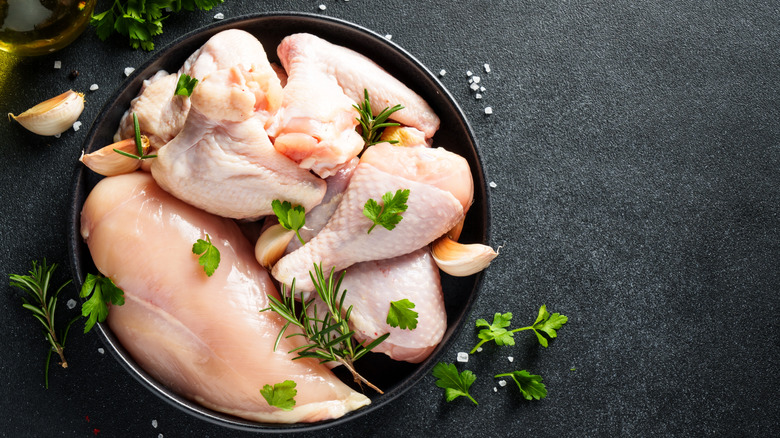 Raw chicken with green herbs in black bowl