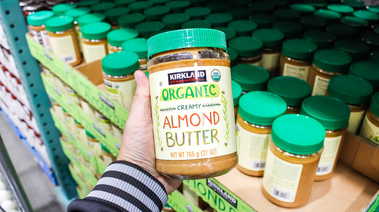 Hand holding jar of organic creamy almond butter in Costco warehouse