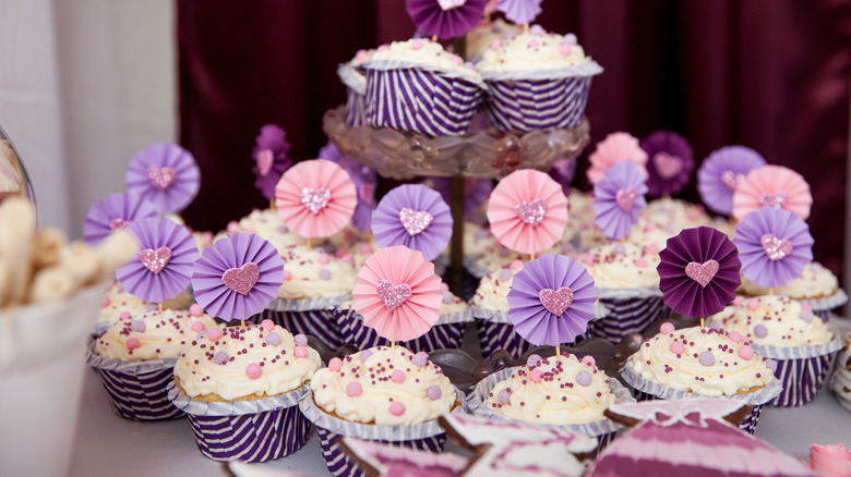 Lots of cupcakes with sprinkles and toppers in shades of purple and pink