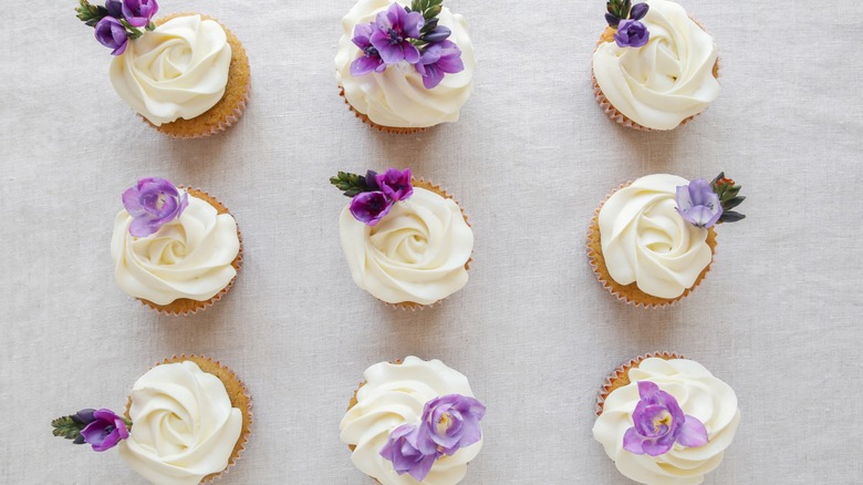 Six cupcakes with white frosting and purple fresh flowers