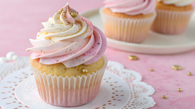 A cupcake with two-tone white and soft pink swirl frosting