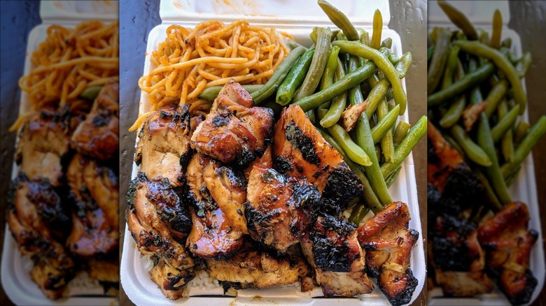 Styrofoam box on a wood table overflowing with spicy noodles, glazed chicken, potatoes, and green beans