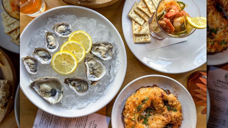 Plate of oysters with lemons on ice, shrimp cocktail with saltine crackers on a white plate, and a crispy baked pretzel on a white plate