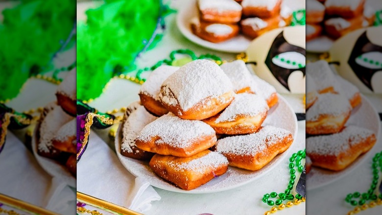 Pile of beignets dusted with copious amounts of powdered sugar sitting on a white plate, with Mardi Gras beads scattered around