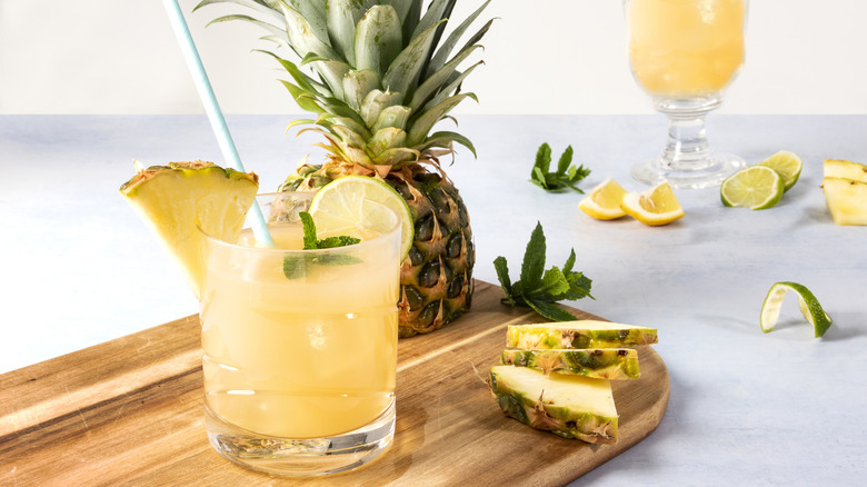 Pineapple juice in rocks glass with whole pineapple and fruit pieces.