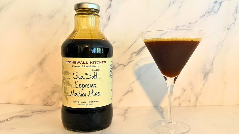 Bottle of Stonewall Kitchen espresso martini mix next to espresso martini in glass on marble surface