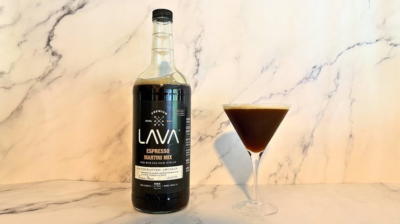 Bottle of Lava espresso martini mix next to espresso martini in glass on marble surface