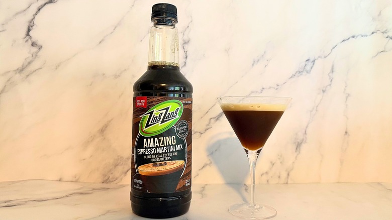 Bottle of Zing Zang espresso martini mix next to espresso martini in glass on marble surface
