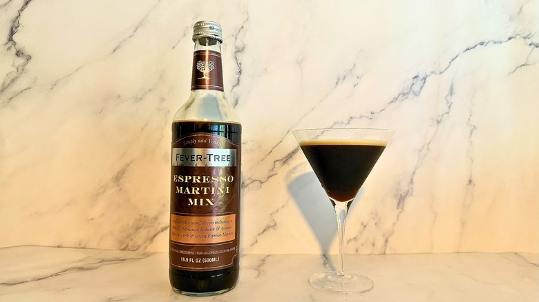 Bottle of Fever-Tree espresso martini mix next to espresso martini in glass on marble surface