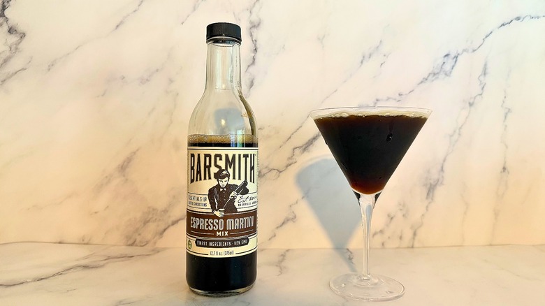 Bottle of Barsmith espresso martini mix next to espresso martini in glass on marble surface