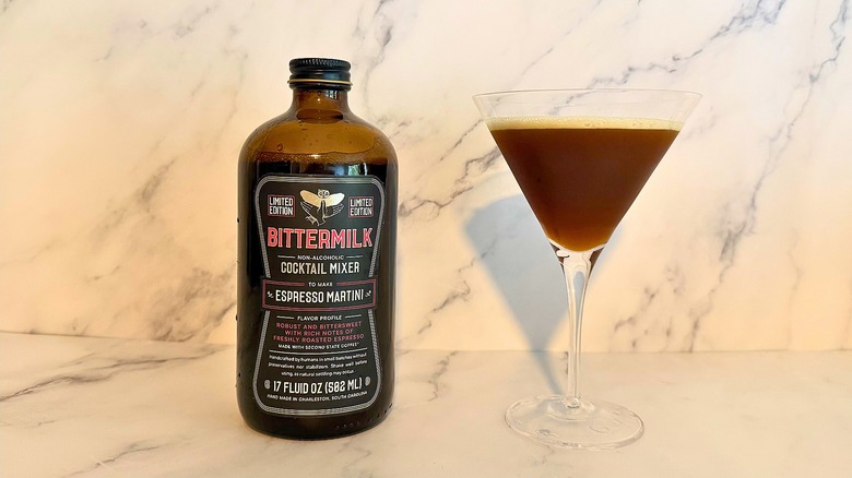 Bottle of Bittermilk espresso martini mix next to espresso martini in glass on marble surface