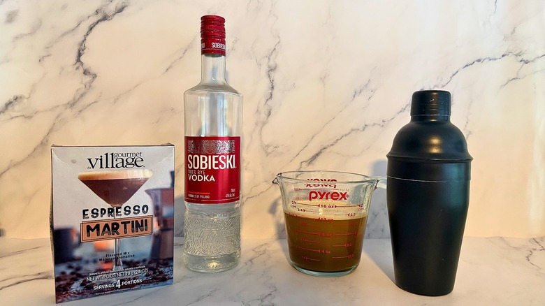 Espresso martini mix, bottle of vodka, pyrex filled with mix and water, and cocktail shaker on marble background