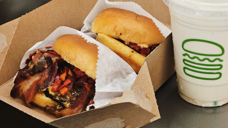 Two Shake Shack burgers in a serving tray next to a beverage