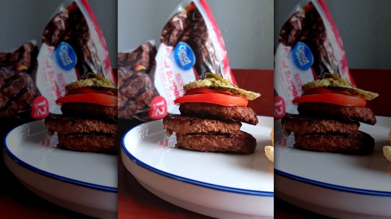 triple burger with tomatoes and pickles on white plate in front of Great Value frozen beef burgers bag