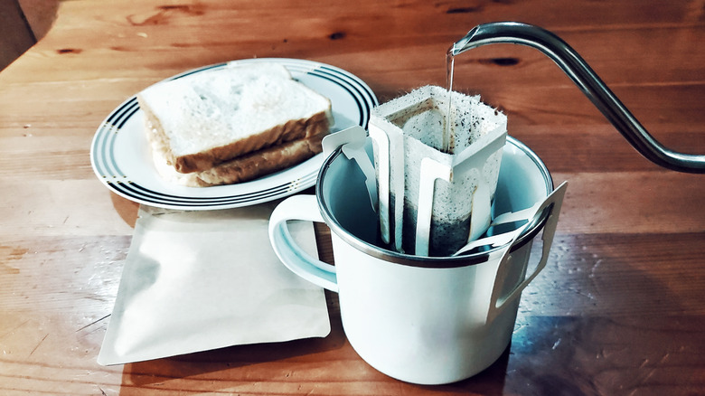 Making a single-serving of pour-over coffee with special filter next to a sandwich on a countertop