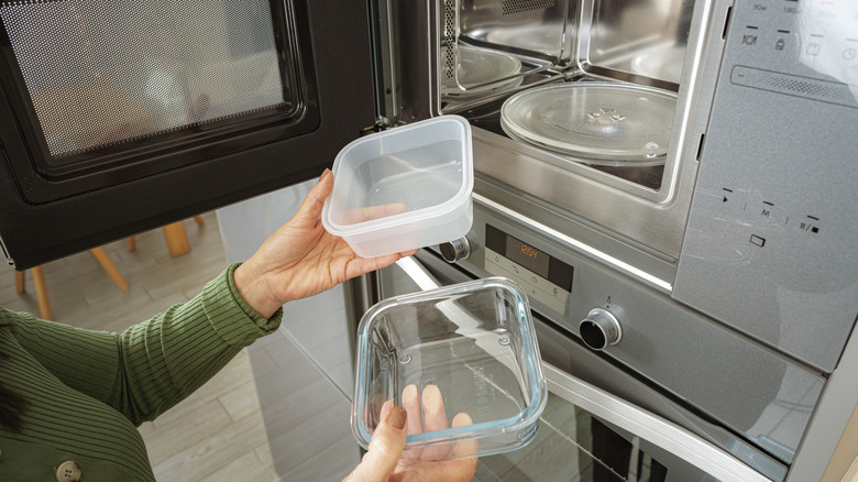 Woman holding empty plastic and empty glass dish in front of microwave