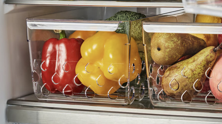 Clear ventilated storage bins filled with bell peppers and pears inside of a refrigerator