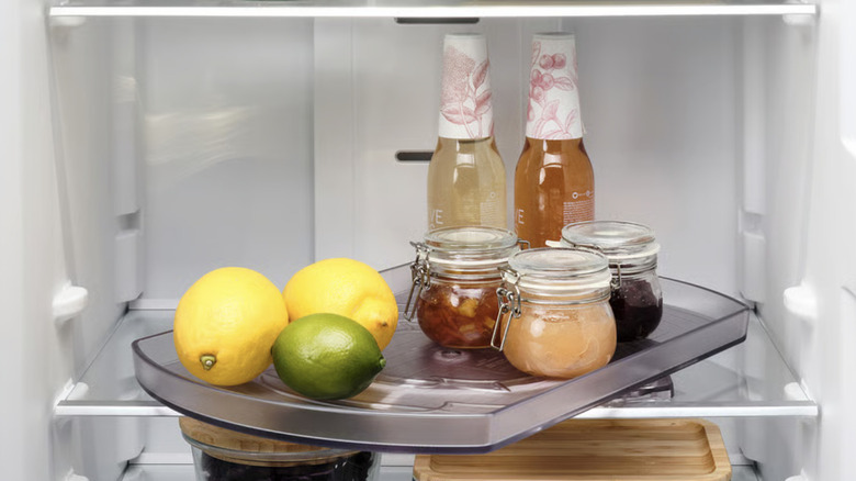 A lazy Susan from Ikea storing lemons, limes, bottles, and small glass containers of food inside of a clean refrigerator
