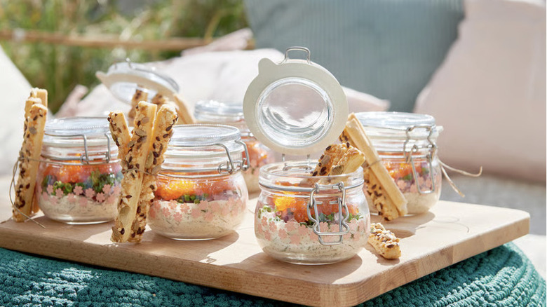 Small glass storage containers being used to serve a spread of dip and crackers outside on a sunny day