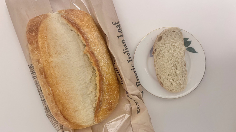 Top view of Bakery rustic Italian bread loaf with one slice on a plate next to it