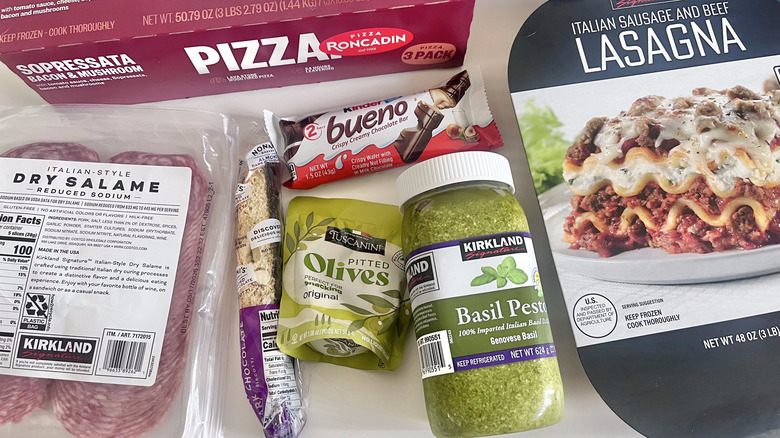 Costco Italian items on a table featuring olives, pizza, salami, lasagna, and Kinder Bueno