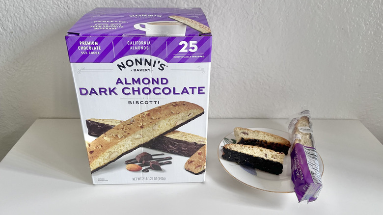 Nonni's dark chocolate almond biscotti broken in half and served on a plate next to the whole box