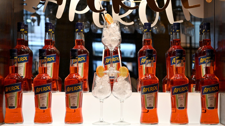 Bottles of Aperol are displayed behind a bar next to a pyramid of ice filled wine glasses.