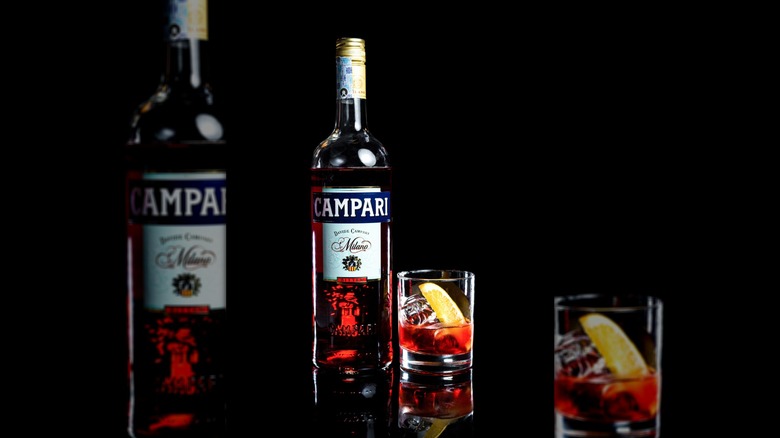 A bottle of Campari and old-fashioned glass against black background.