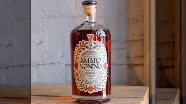 Bottle of Nonino Quintessentia on wood table against white brick wall.