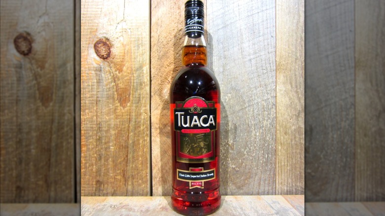 Bottle of Tuaca against a panel wall.
