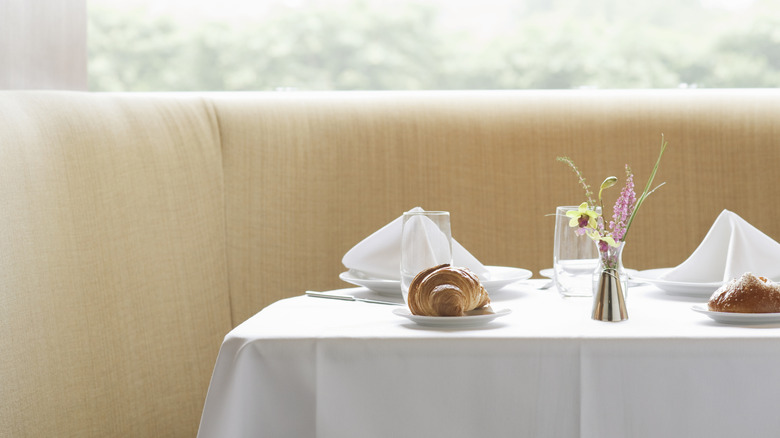 Restaurant seating and table with tablecloth, napkins, plates, and flowers