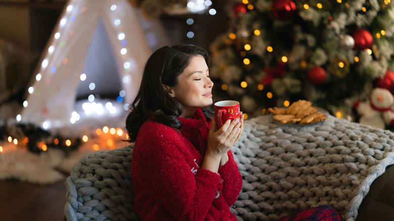 Woman enjoying a warm drink on a sofa next to a Christmas tree