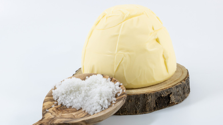 Mound of butter on a wooden plate with a spoon of salt