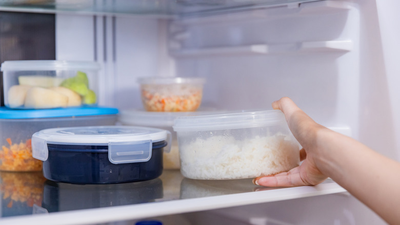 Hand putting plastic container of leftover rice in the fridge