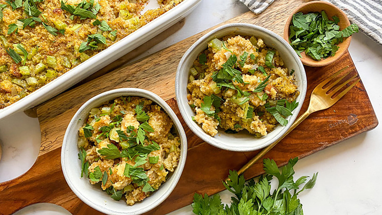 Cornbread dressing in baking dish and two bowls, garnished with fresh parsley