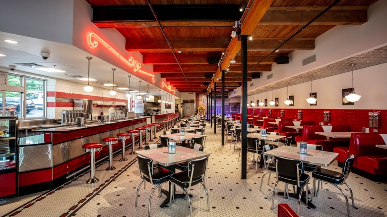 Interior of soda fountain with red booths and stools, counter, and black and white tables and chairs