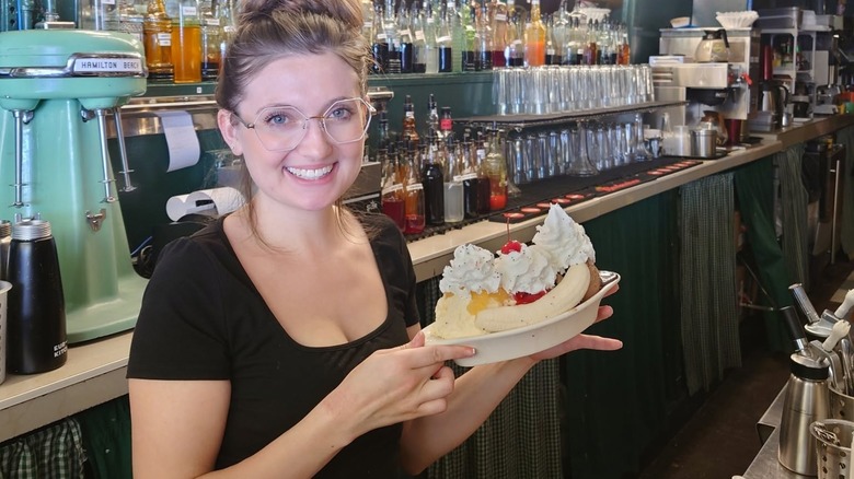 Smiling employee holding a banana split behind counter
